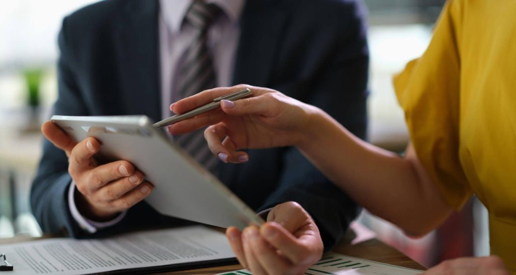 Two professionals reviewing cost breakdown on tablet while calculating Amazon referral fees and seller costs